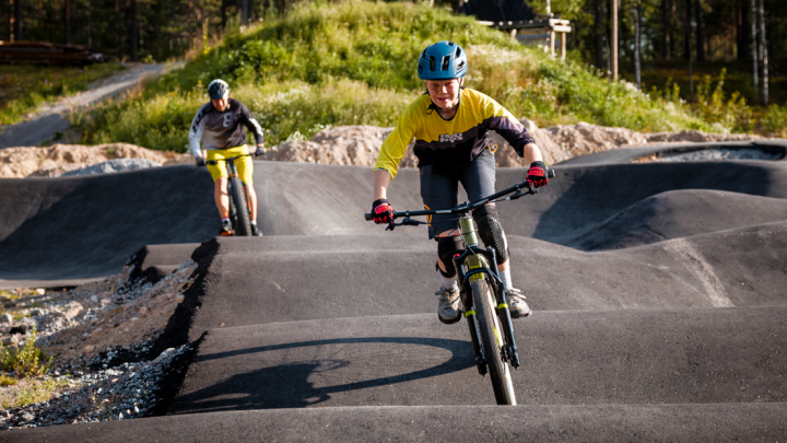 Kaksi pyöräilijää asfaltoidulla pumptrack-radalla.